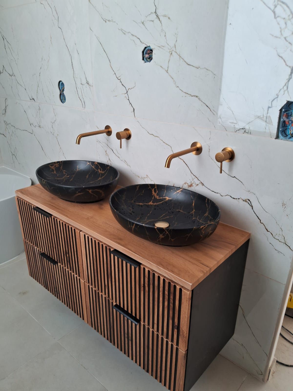 Salle de bain rénovée avec meuble double vasque en marbre noir et robinetterie dorée